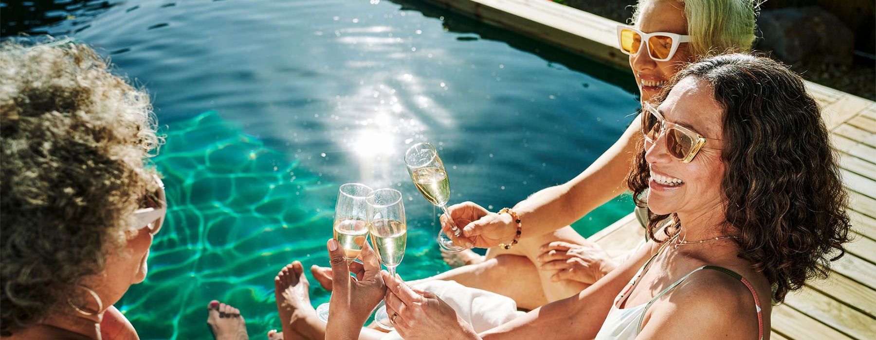 a group of women sitting by a pool with drinks